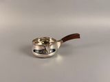 une casserole en argent avec un manche en bois posée sur une surface blanche