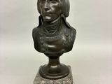 un buste en bronze représentant un homme aux cheveux longs, posé sur un socle en marbre