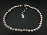 un collier de perles blanches muni d'un fermoir en argent, sur fond noir