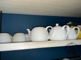 several white teapots are lined up on a shelf in a kitchen