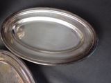 two silver oval trays on a table with a black background