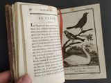 a hand holding an open book with a picture of a bird on it