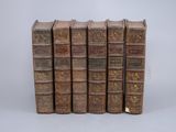 five old books lined up in a row on a white surface