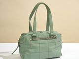 green quilted handbag with metal handles on a white table