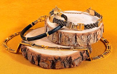 two bracelets with black and gold beads on a wooden stand