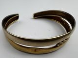 gold tone cuff bracelet with curved design on white background