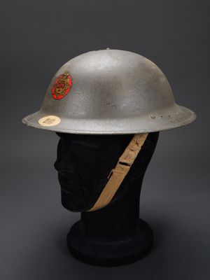 un casque argenté posé sur une tête de mannequin, orné d'un insigne rouge
