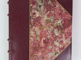 an old book with a red cover and gold trim on a white surface
