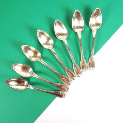 six cuillères en argent sont disposées en cercle sur un fond vert et blanc