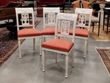 four white chairs with red upholstered cushions sit in a room