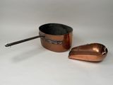 une petite casserole en cuivre et une cuillère posées sur une surface blanche