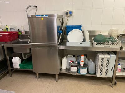 un grand évier en inox dans une cuisine où l'on trouve de nombreux produits d'entretien