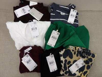 six paires de t-shirts posées sur un canapé, avec leurs étiquettes de prix