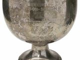 une coupe en argent ancienne posée sur un socle, sur fond blanc