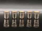 six silver shot glasses lined up in a row on a black surface