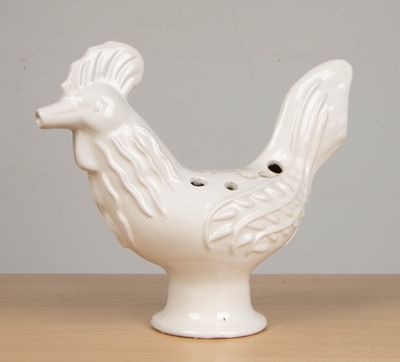 un coq en céramique blanche posé sur une table, sur fond gris