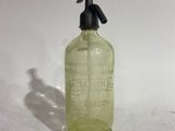 an old green glass bottle with a black handle on a white surface