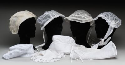 trois mannequins coiffés de chapeaux et vêtus de tissus blancs, posés sur une table
