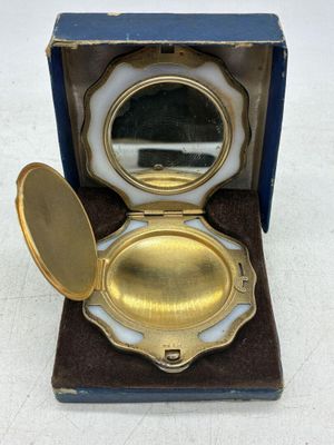 miroir de poche plaqué or dans un écrin bleu posé sur une surface blanche