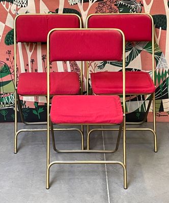 four red chairs sitting next to each other in front of a wall