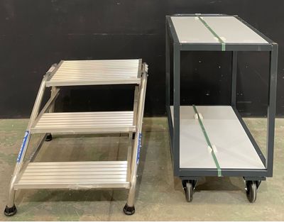 pair of two aluminum step stools with wheels and a shelf