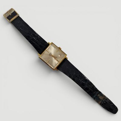 gros plan d'une montre sur une surface blanche avec un bracelet noir