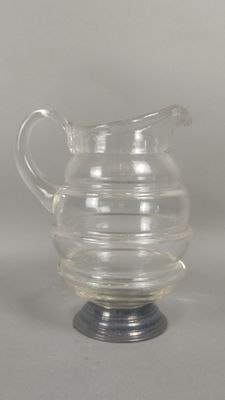 une image représentant un pichet en verre transparent posé sur un support métallique