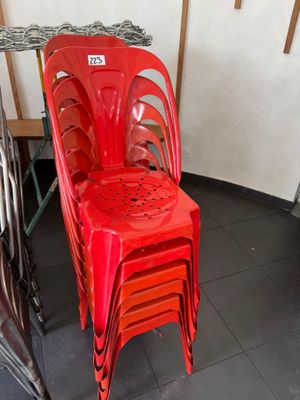 a red plastic chair sitting next to a stack of chairs