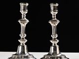 une paire de bougeoirs en argent posés sur une table blanche, sur fond noir