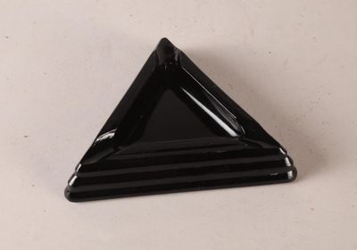un objet en verre noir de forme triangulaire posé sur une surface blanche