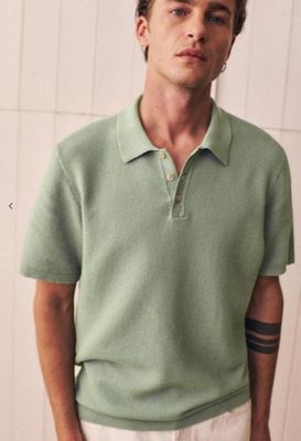 a man standing in front of a white wall wearing a green shirt and white pants
