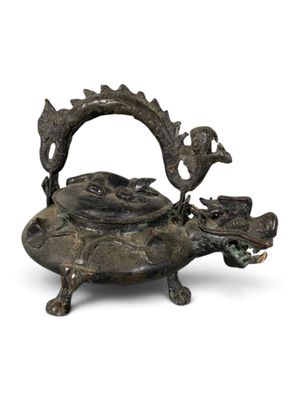 une vieille théière en bronze avec une anse en forme de dragon sur fond blanc