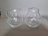 two glass pitchers sitting on a table next to each other
