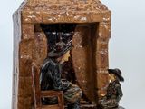 une figurine représentant un homme et une femme assis devant un bâtiment en pierre