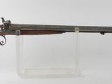 un vieux pistolet au canon en bois, exposé sur un support blanc