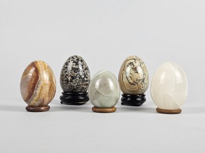 un ensemble de cinq œufs en marbre posés sur un socle en bois