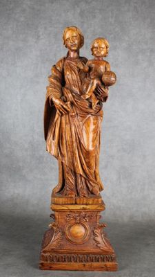 une statue en bois représentant une femme tenant un enfant dans ses bras, posée sur un socle