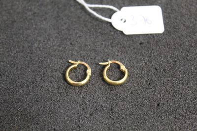 une paire de petites boucles d'oreilles en or en forme d'anneaux sur un fond noir