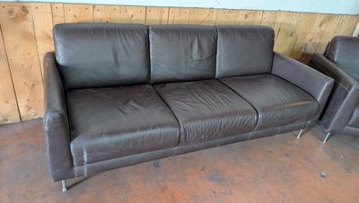 un canapé en cuir marron et deux fauteuils dans une pièce