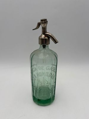 an old green glass bottle with a metal spout on a white surface