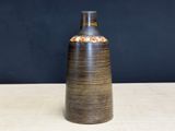 un vase marron posé sur une table, avec un mur noir en arrière-plan