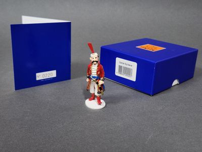 La figurine se tient à côté d'une boîte bleue et d'un soldat rouge et blanc.