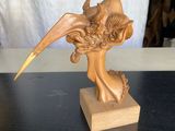 statue représentant une femme avec un oiseau sur la tête, posée sur un socle en bois