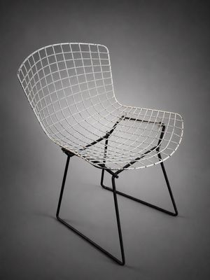 une photo en noir et blanc d'une chaise en fil de fer sur fond gris