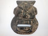 un masque en métal accroché à un mur sur fond blanc