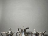 three silver teapots and a coffee pot sitting on a table