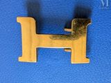 a gold metal letter h on a blue leather surface