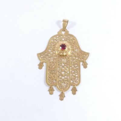 un pendentif en forme de hamsa en or, orné d'une pierre rouge au centre