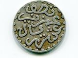 une vieille pièce de monnaie portant une inscription en arabe, posée sur une surface blanche