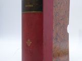an old book sitting on top of a white surface with a red cover